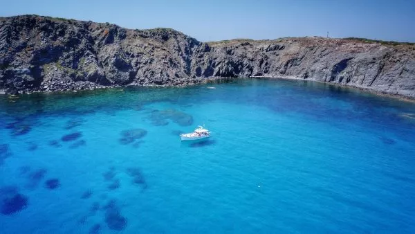 Llaut anchored in a turquoise cove surrounded by cliffs in Menorca